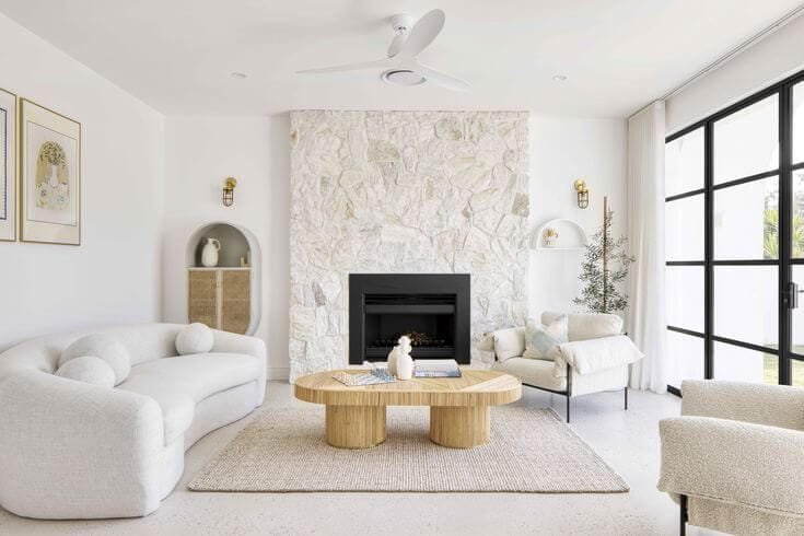 a light bright white living room with stone fireplace on one wall 